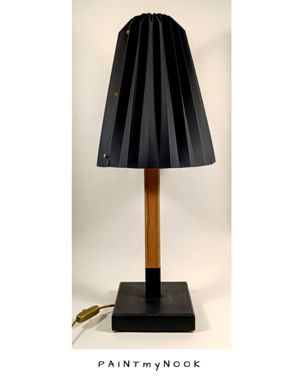 A table lamp with black origami lampshade and wooden base partly colored black