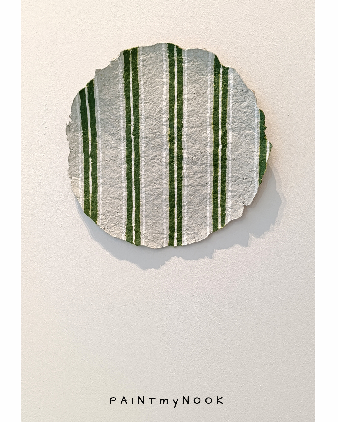 A paper mache decorative plate with green stripes painted on it