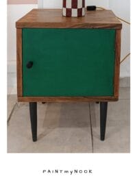 A wooden upcycled bedside table with a green colored door and black legs.