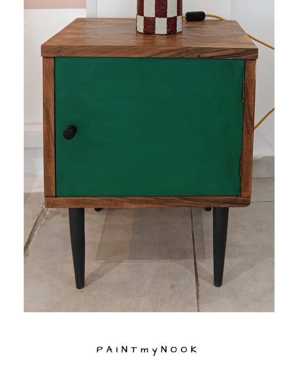 A wooden upcycled bedside table with a green colored door and black legs.