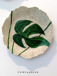 A decorative papier mache plate with a monstera leaf painted in green color