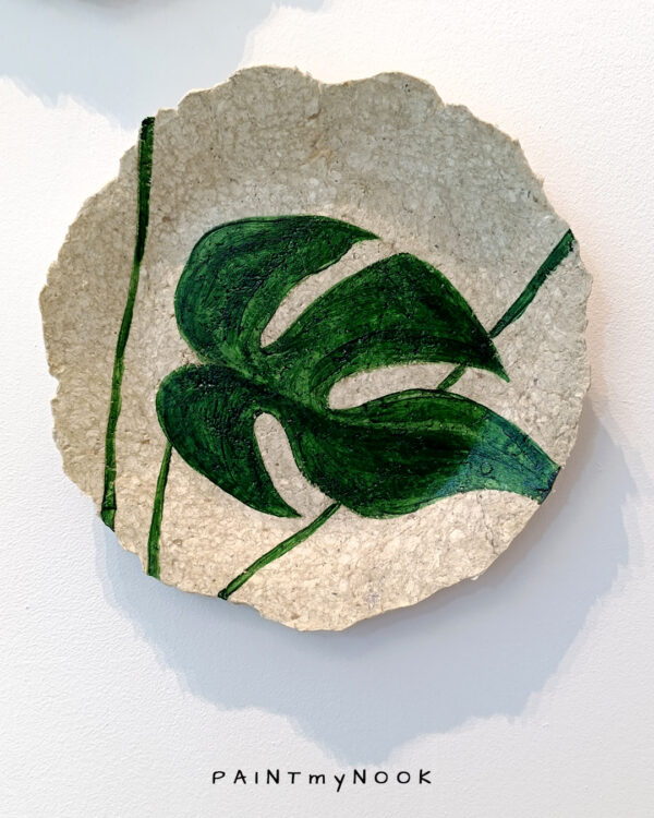 A decorative papier mache plate with a monstera leaf painted in green color