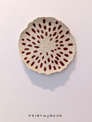 A paper mache decorative plate with red seeds painted on it