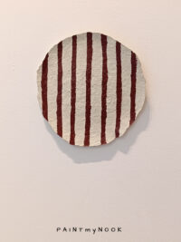 A paper mache decorative plate with red stripes painted on it