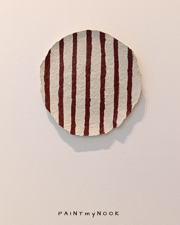 A paper mache decorative plate with red stripes painted on it