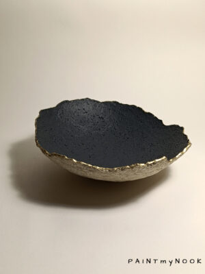 A papier mache bowl with a gold rim and black concave side