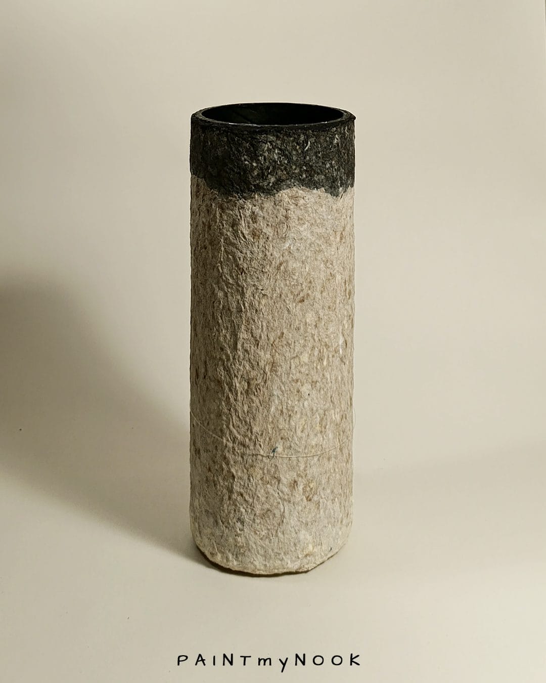 A beige and grey cylindrical papier mache vase