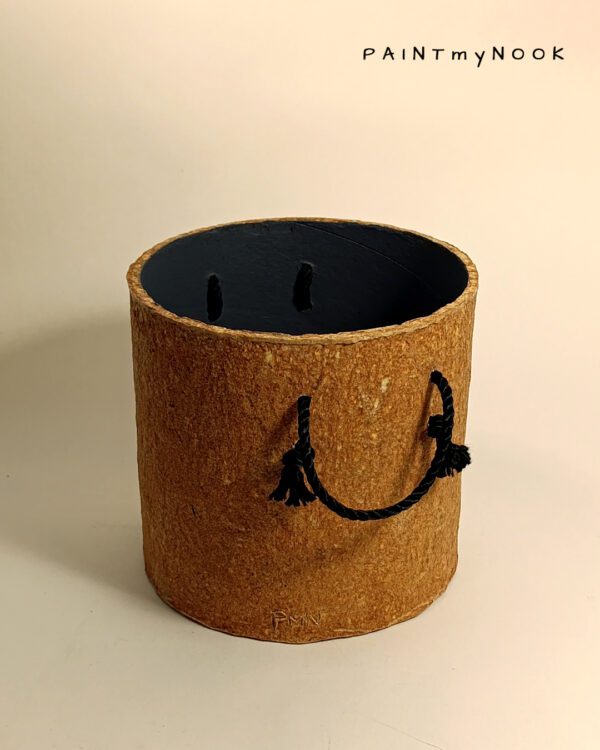 A cylindrical, orange colored papier mache planter cover