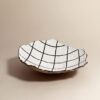 A white papier mache bowl with a grid drawing