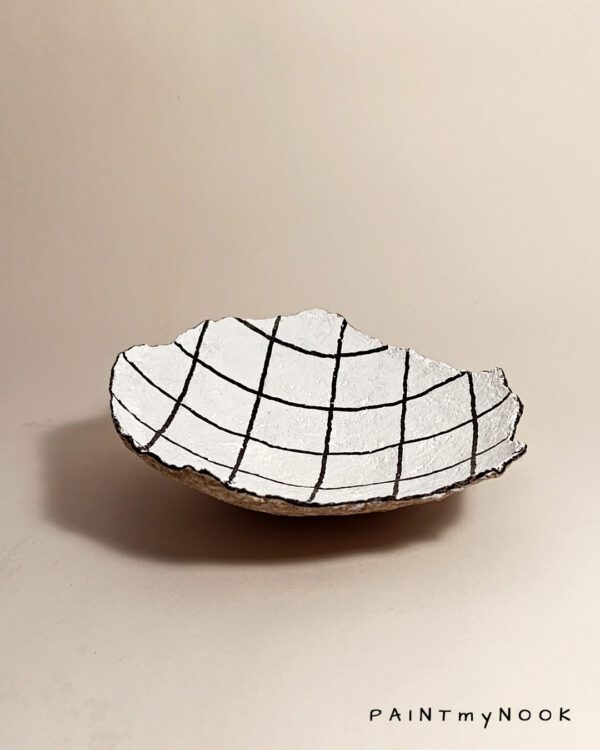 A white papier mache bowl with a grid drawing