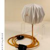 A white paper lamp folded using origami techniques, attached to a transparent plexiglass prop, with a mustard yellow textile cable