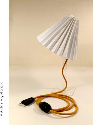A table top white origami paper lamp with a mustard yellow textile cable on a transparent plexiglas prop.