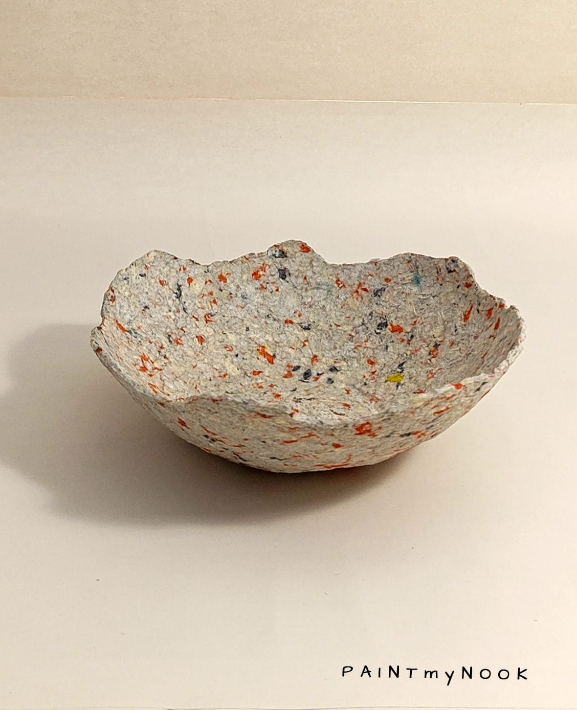 A beige papier mache bowl with orange details