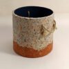 A beige and orange planter cover with rope handles made of paper pulp.