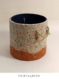 A beige and orange planter cover with rope handles made of paper pulp.