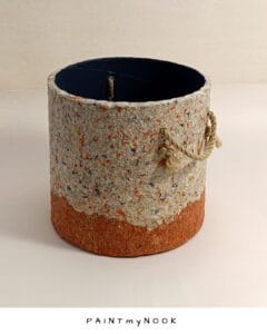 A beige and orange planter cover with rope handles made of paper pulp.