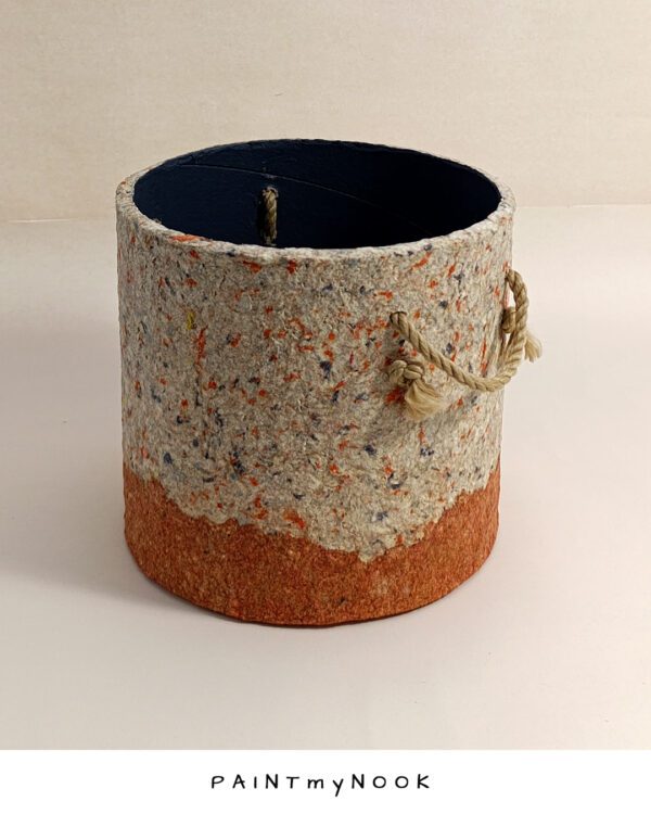 A beige and orange planter cover with rope handles made of paper pulp.