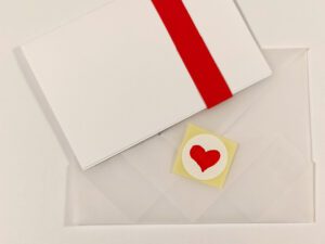 A white envelope with red paper band, an envelope and a heart sticker