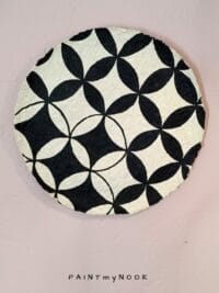 A beige papier mache decorative plate with black quatrefoil pattern painted on.