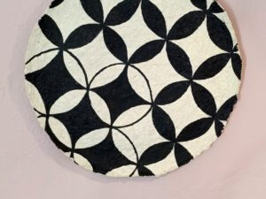 A beige papier mache decorative plate with black quatrefoil pattern painted on.