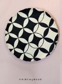 A beige papier mache decorative plate with black quatrefoil pattern painted on.