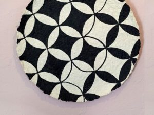 A beige papier mache decorative plate with black quatrefoil pattern painted on.