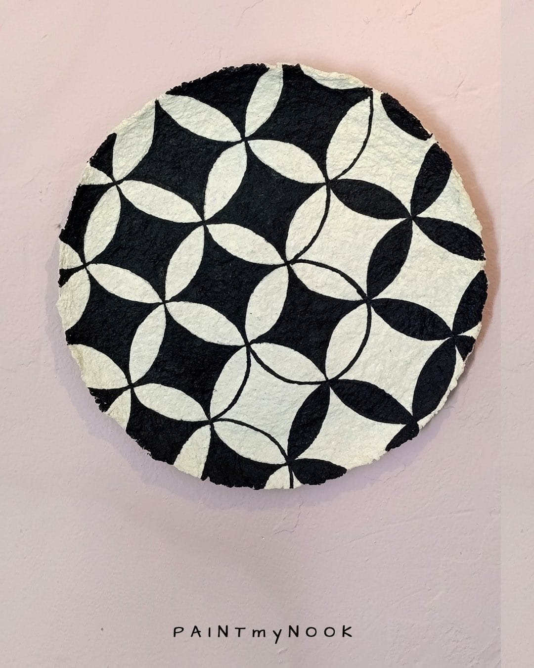 A beige papier mache decorative plate with black quatrefoil pattern painted on.